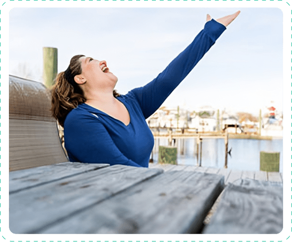 Woman joyfully reaches upward by waterfront