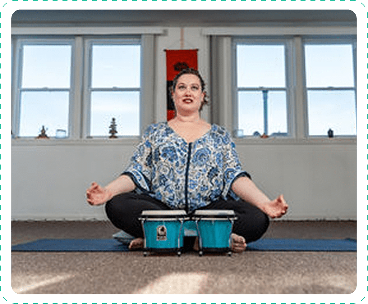 Woman meditating indoors with bongo drums in front of her.