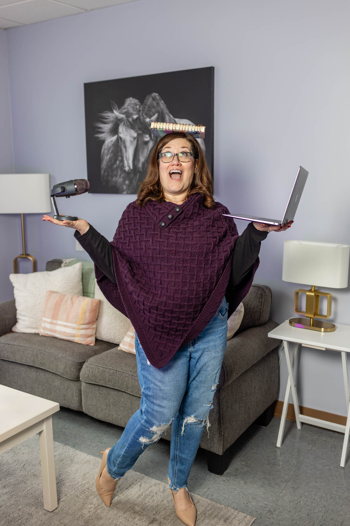 A woman happily holding a laptop and a book in a cozy living room.