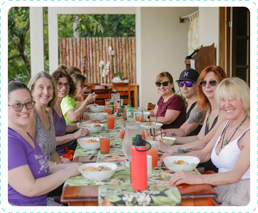 Group of women enjoying a meal together outdoors at a long wooden table.