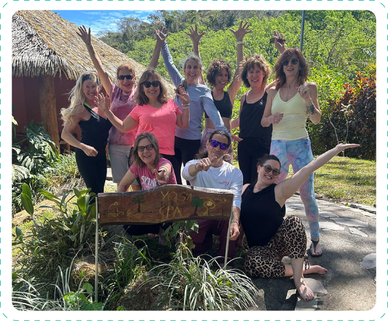 Group of women posing happily outdoors with a wooden sign.